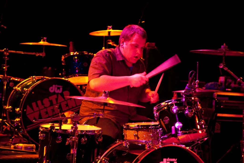 The drummer mid-song with sticks raised, lit in red