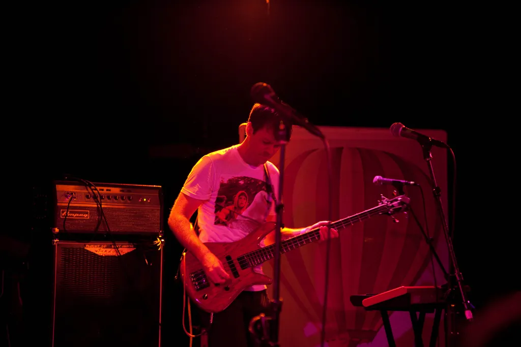 The guitarist playing in red stage light beside an amplifier
